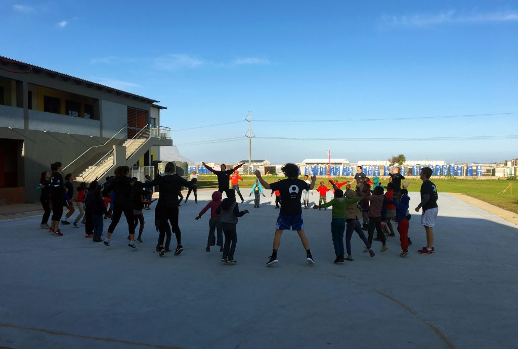 student athletes and kids playing game in circle outside