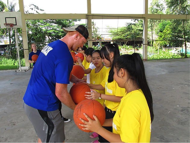 Young man helping girls properly hold a basketball