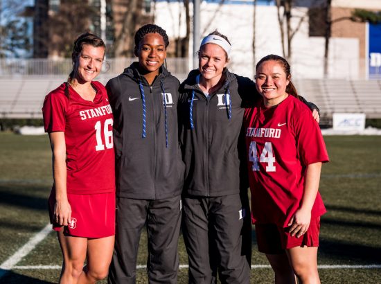 four women posing together on a lacrosse field
