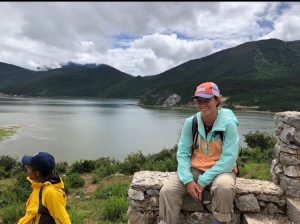 student smiling wearing a baseball hat in front of a lake and mountains