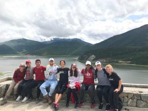 nine duke and stanford student-athletes sitting in front of a lake and mountains