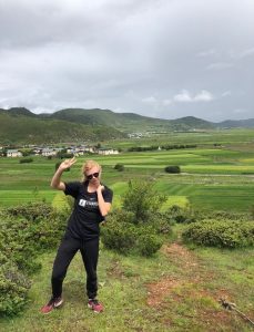 student smiling wearing sunglasses in front of a green field and mountains