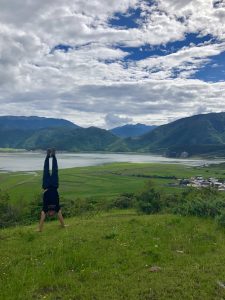 male doing handstand on grassy field with mountains and lake in background