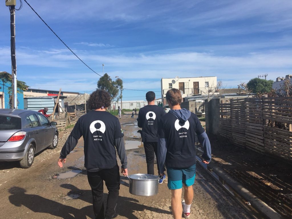 three students carrying big metal pots of food