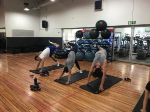 three students doing yoga poses in a gym