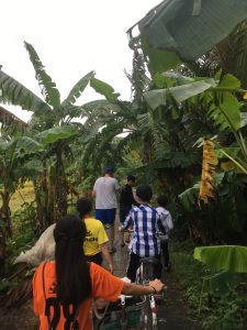 four students on bikes and walking through dense vegetation