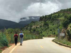 two men walking alongside a road with mountains in the distance