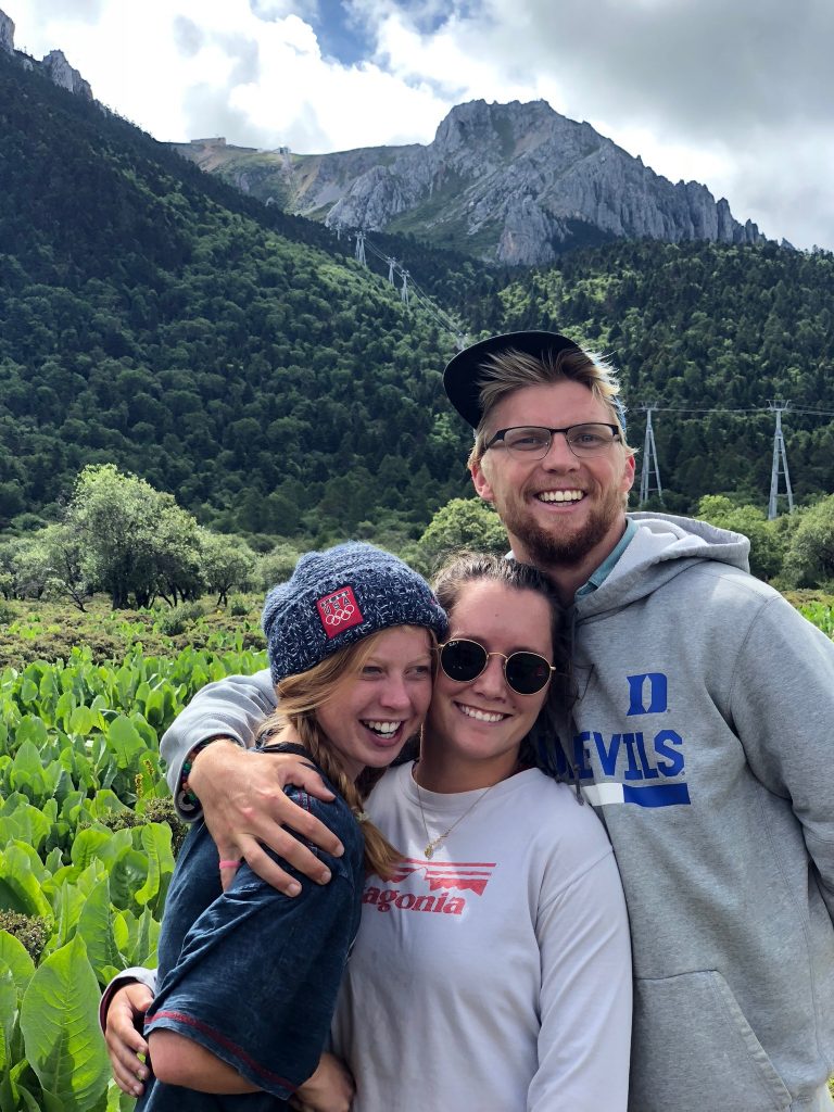 three students with arms around each other mountain in background