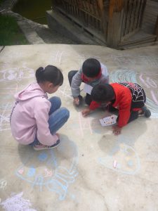 three kids drawing on sidewalk with chalk