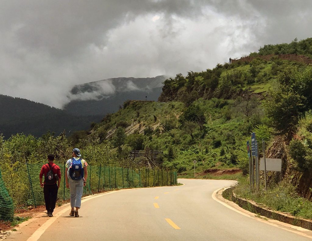 two men with backpacks on walking along a mountainous road