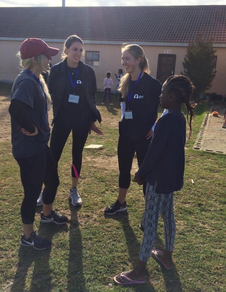 female student-athletes talking to child outside at camp