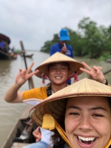 young adults in kayak posing for selfie with vietnamese hats on