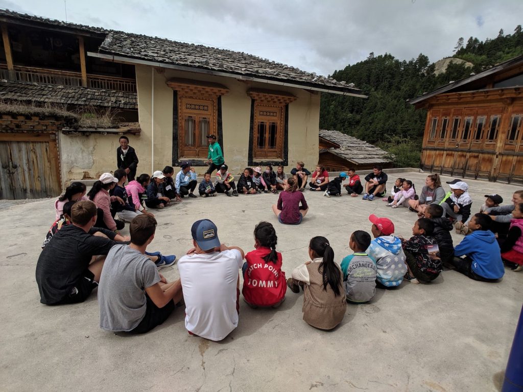 group of kids and young adults sitting in a circle outside