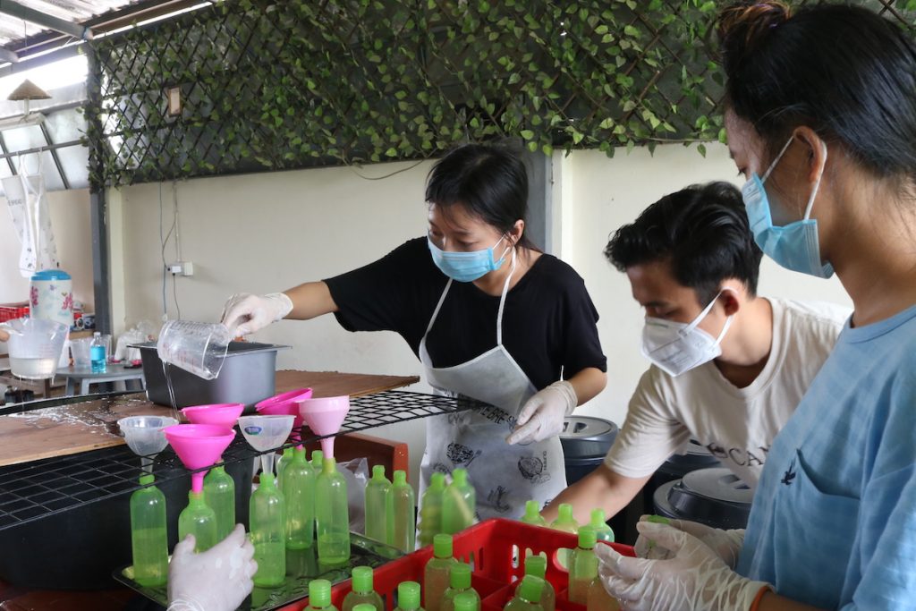 people wearing masks filling up soap bottles using funnel