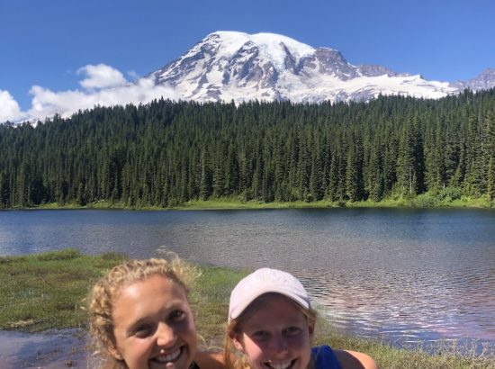two women smiling in front of snowy mountain and lake